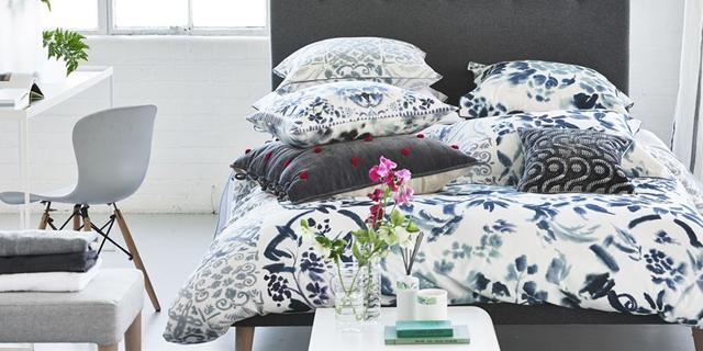 An image of a corner bedroom with a desk and a bed with a black and white devut